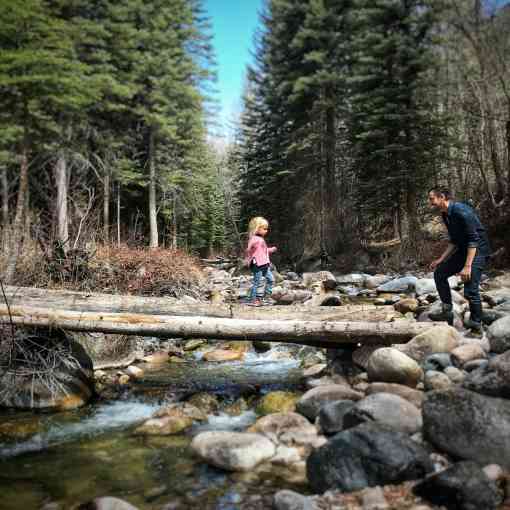 Dad and daughter hiking through woods across river