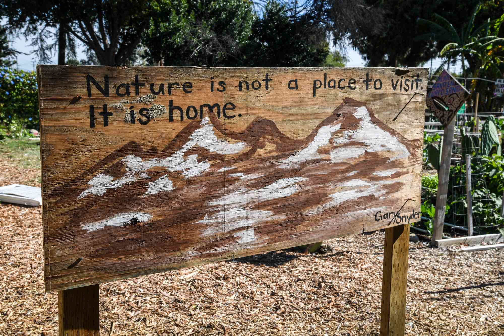 A painting by Siu Luna and Gary Snyder's quote "Nature is not a place to visit. It is home." stands in the community garden plots Ontario, California